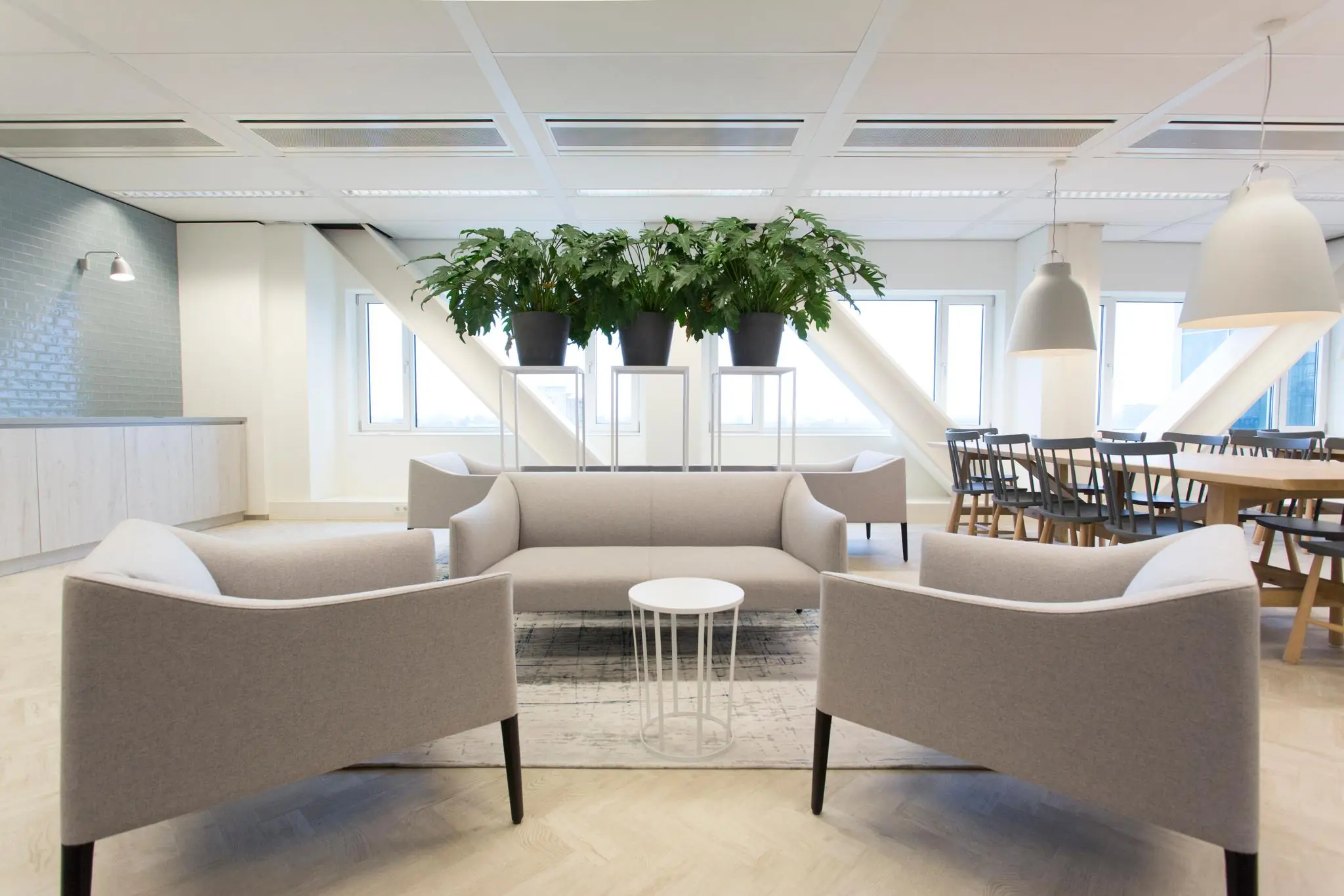 Moderne wachtruimte aan het Rivium Boulevard met grijze zitmeubels, grote planten en houten eetgedeelte.